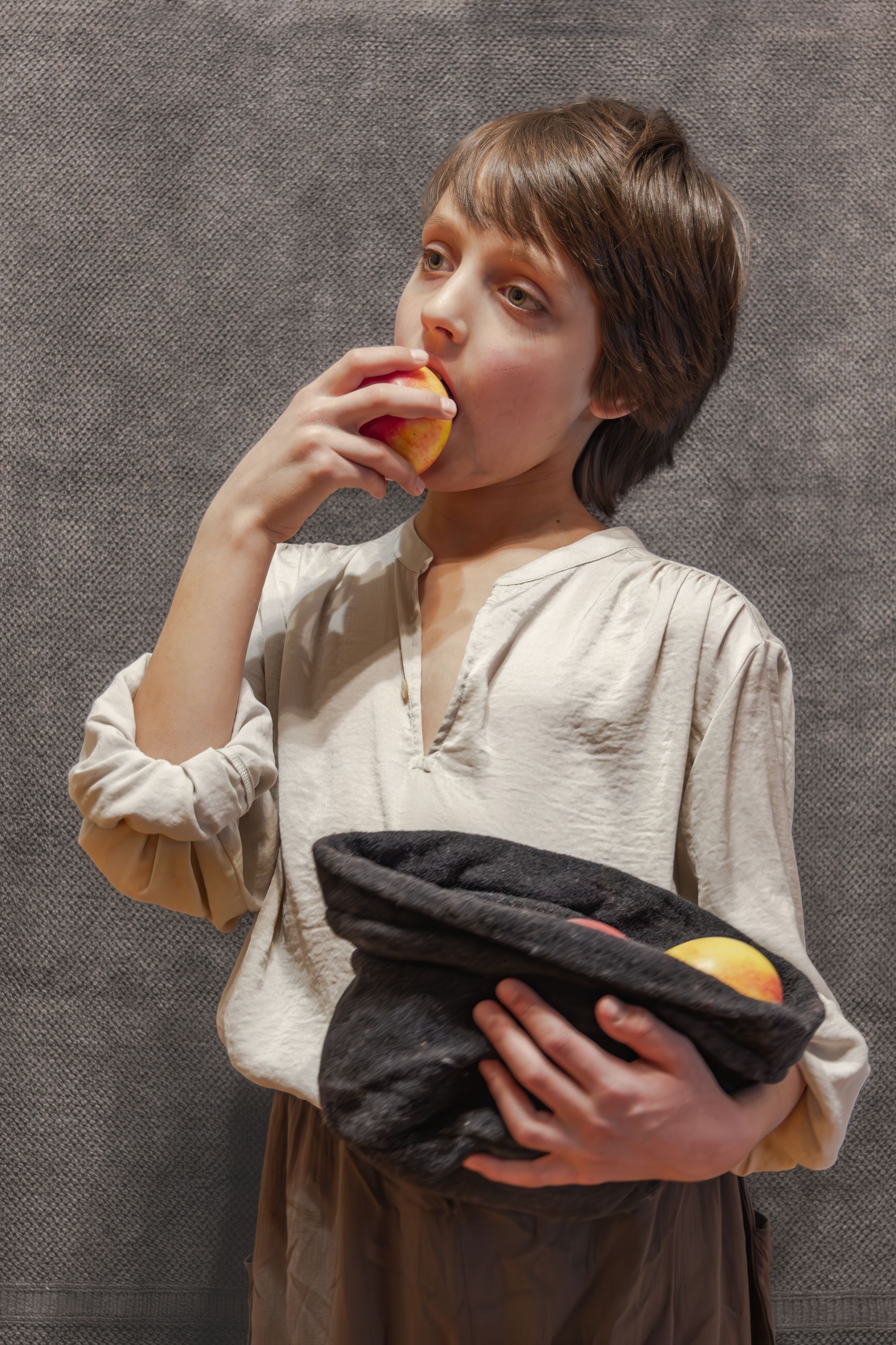 Young boy in rustic attire biting a peach, conveying simplicity and innocence.