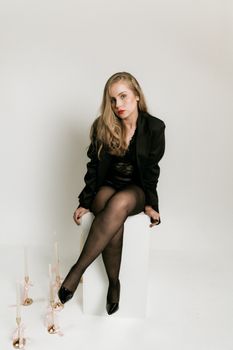 Elegant woman in black attire sitting in a minimalist indoor setting with candles.