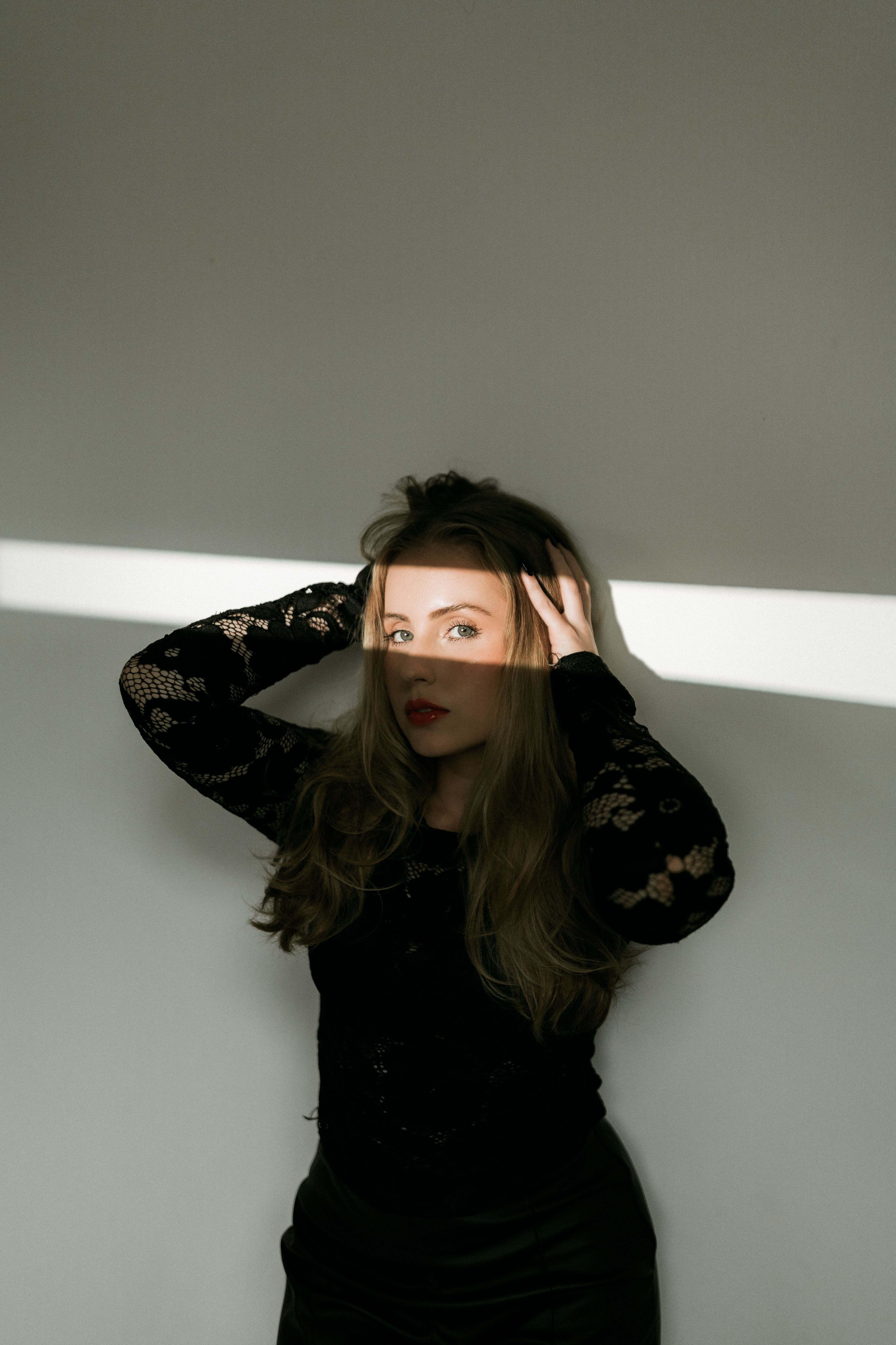 Woman posing in dramatic light with shadow pattern on face, showcasing elegance.