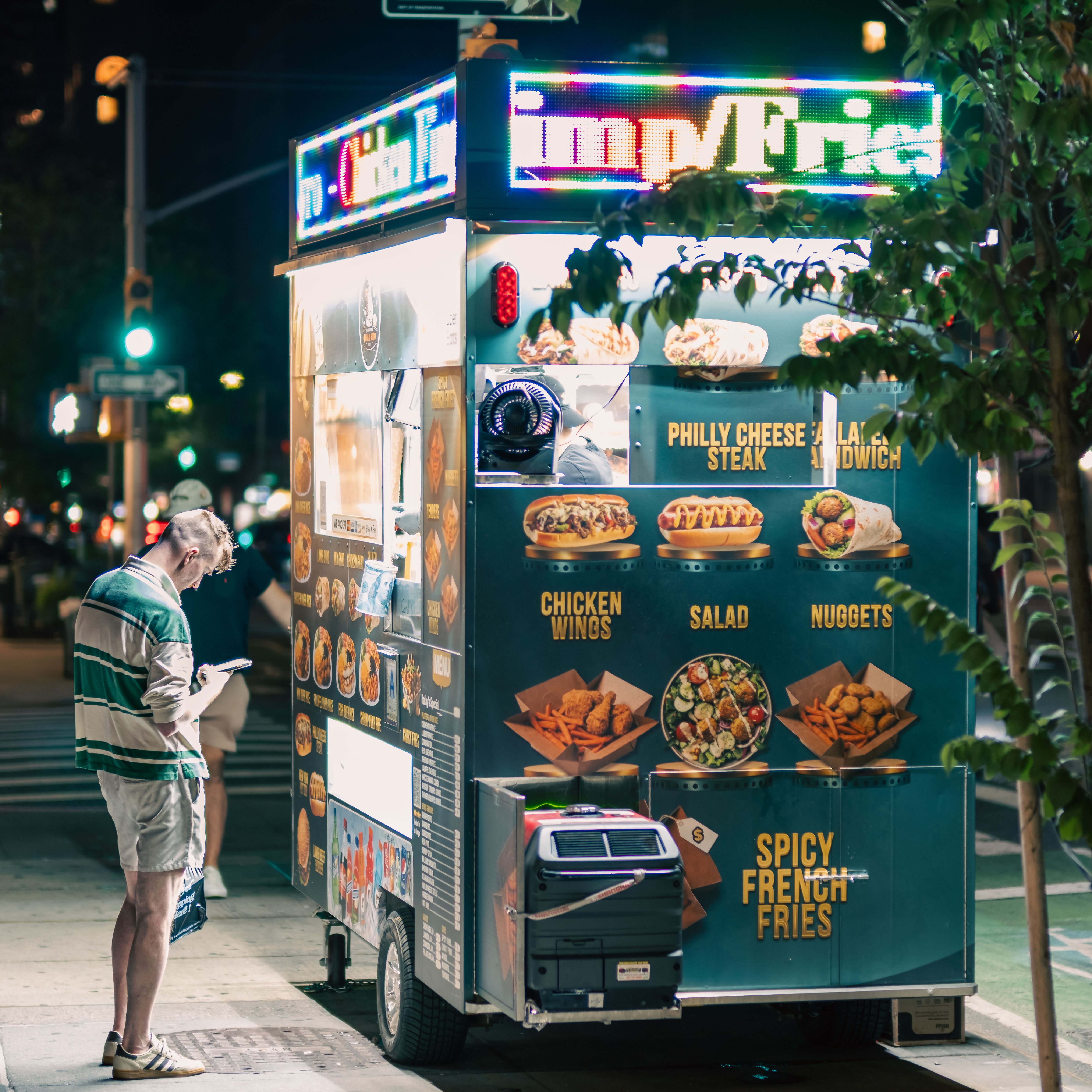 A lively street food cart in New York City, glowing with neon lights, attracting a pedestrian in the night.