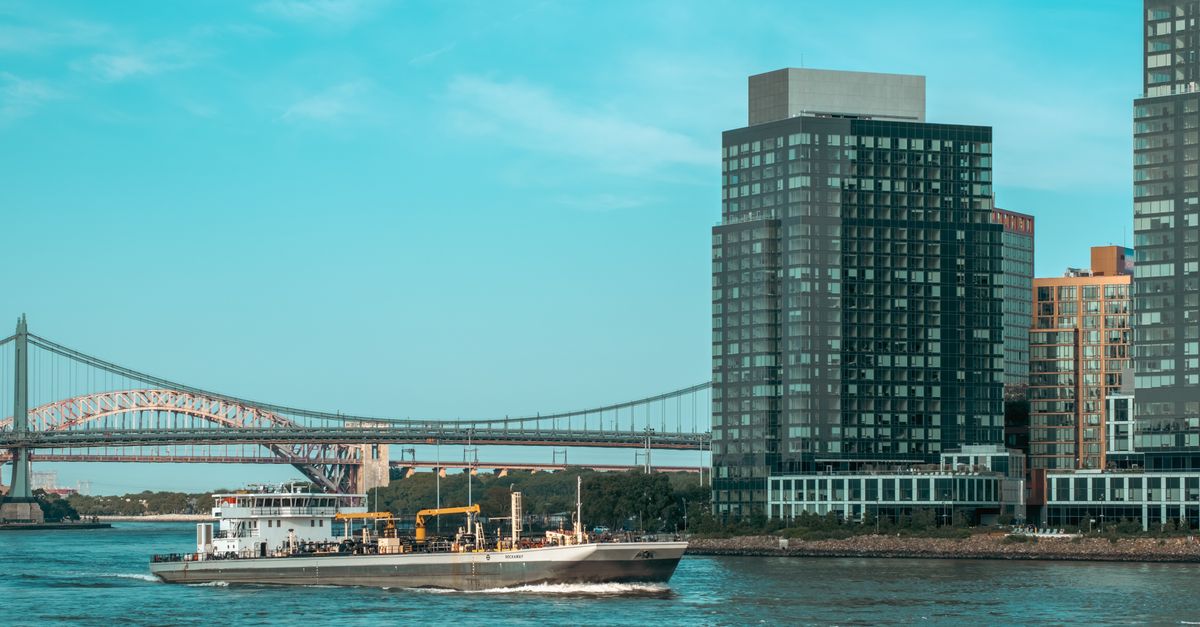 Scenic view of New York City waterfront with skyscrapers and bridge under a clear blue sky.