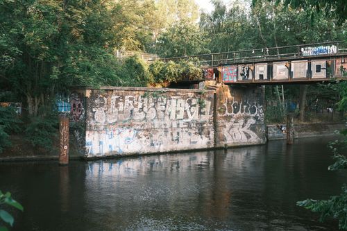Free Graffiti-covered railway bridge over a river with lush greenery in Berlin, Germany. Stock Photo