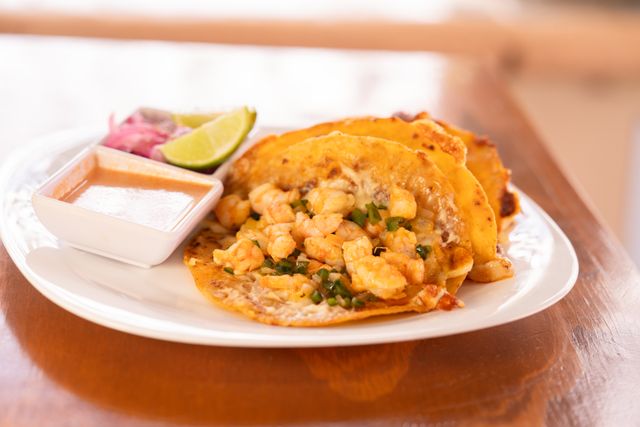 A mouthwatering plate of shrimp tacos served with lime wedges and dipping sauce on a white plate.