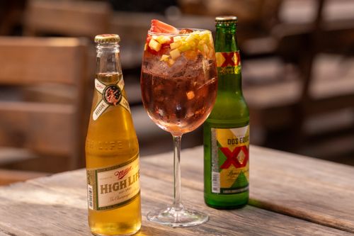 Free A colorful cocktail with fresh fruit alongside two beer bottles on a rustic table setting indoors. Stock Photo