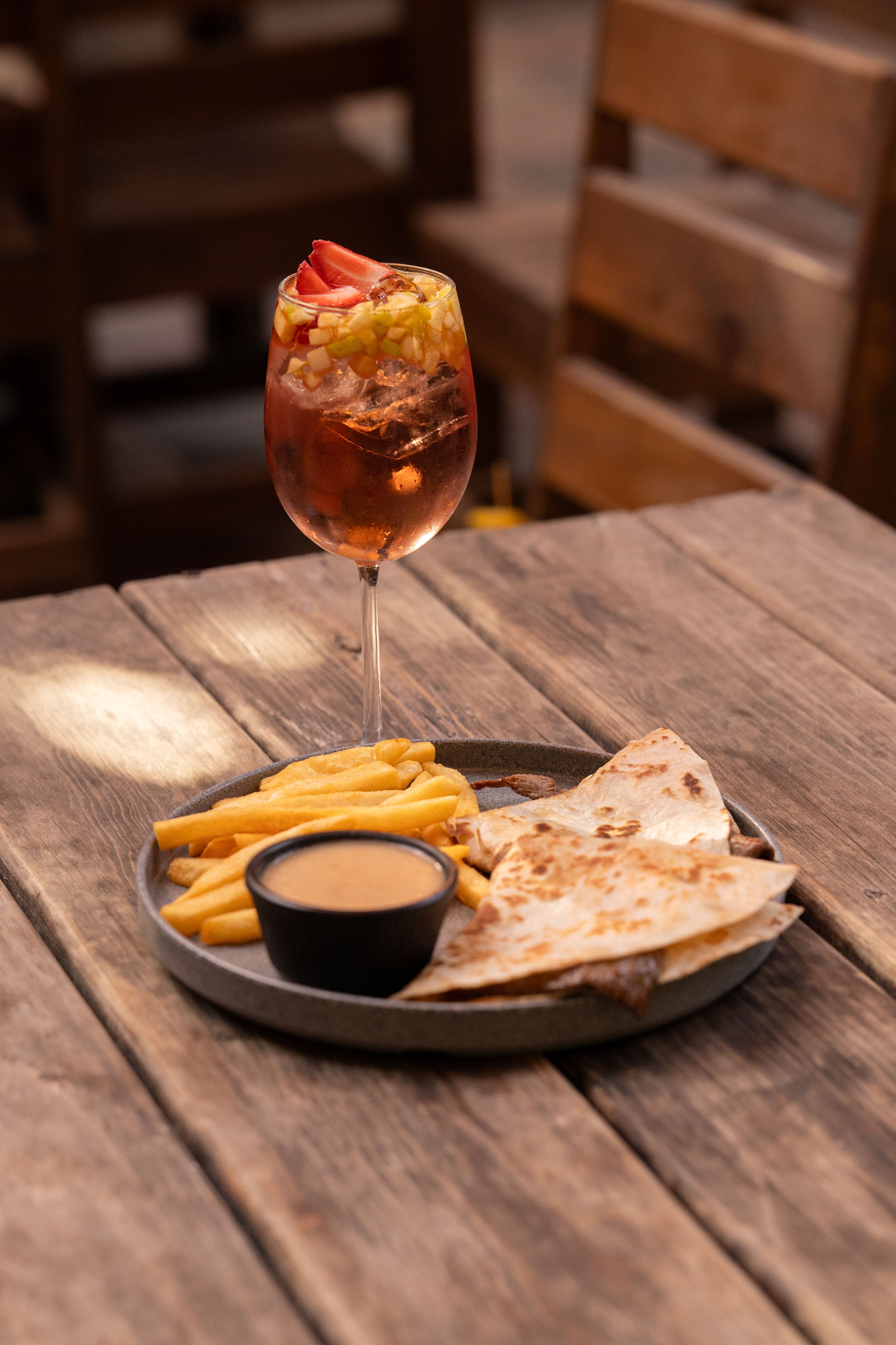 A quesadilla, fries, and cocktail on a wooden table, outdoors.