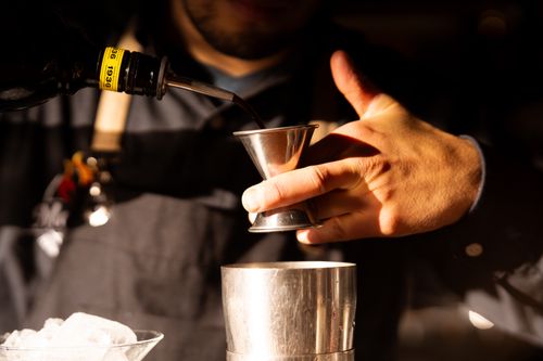Free Close-up of a bartender pouring a drink using a jigger, showcasing cocktail-making skills in a cozy atmosphere. Stock Photo