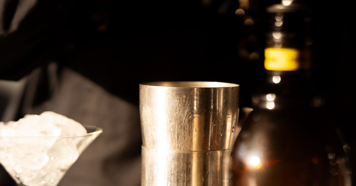 Close-up of cocktail preparation with shaker, ice, and bottle.