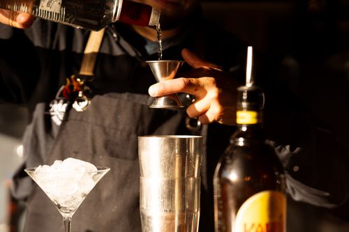 Free A bartender carefully pouring liquor into a jigger, surrounded by cocktail-making tools as warm light highlights the setting. Stock Photo