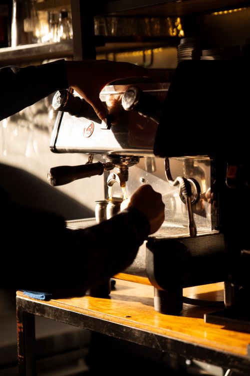 Free Silhouette of a barista making espresso using a coffee machine in a cozy café with warm lighting. Stock Photo