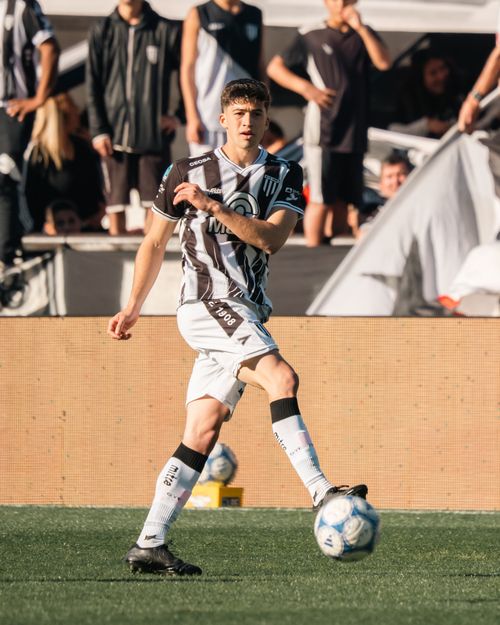Free Male soccer player in striped jersey kicking ball during a match on sunny day. Stock Photo