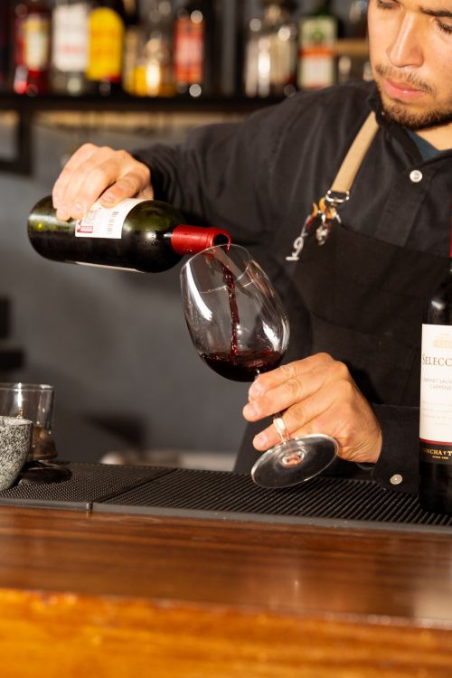 Free A bartender gracefully pouring red wine into a glass, showcasing attentive service and fine wine selection. Stock Photo
