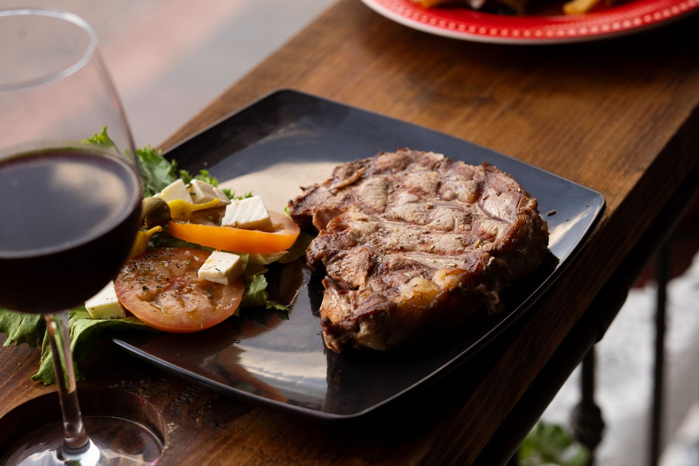 Grilled bone-in chop with a glass of red wine on a wooden table, the live-fire pairing driving Pennsylvania fall menus