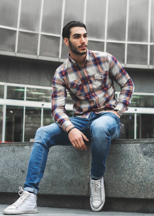 격자 무늬 셔츠와 블루 데님 청바지 콘크리트에 앉아있는 남자