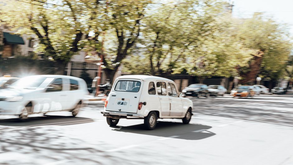 Classic white car driving on a sunny day in Mendoza, Argentina streets.