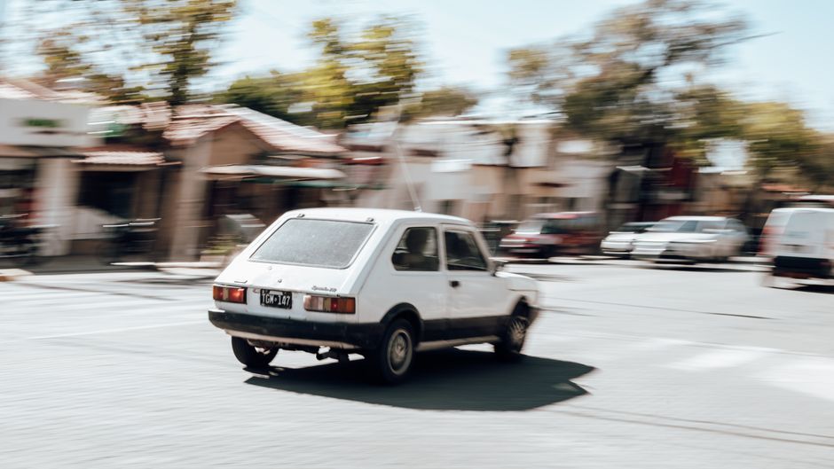 A white vintage car in motion on a sunny street in Mendoza, Argentina. Blurred background effect.