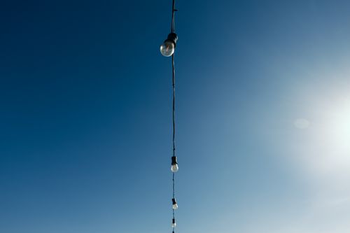 Free Minimalistic view of string lights hanging against the bright blue sky with the sun shining. Stock Photo