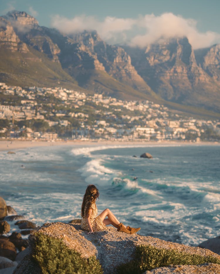 Woman Sitting On Rock Near Body Of Water