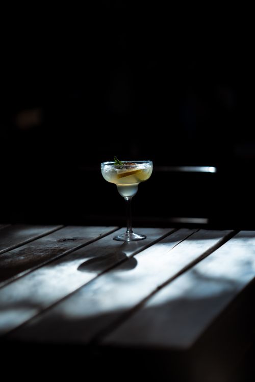 Free A sophisticated cocktail garnished with herbs sits elegantly on a rustic wooden table under striking lighting. Stock Photo