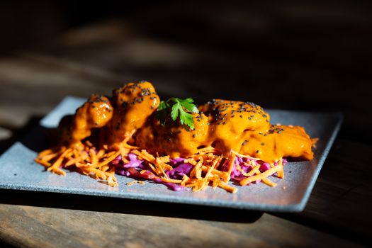 Spicy gochujang chicken garnished with black sesame seeds served on a bed of slaw.