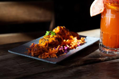 Free Close-up of a gourmet dish with vibrant garnish and a spicy cocktail served on a rustic wooden table. Stock Photo