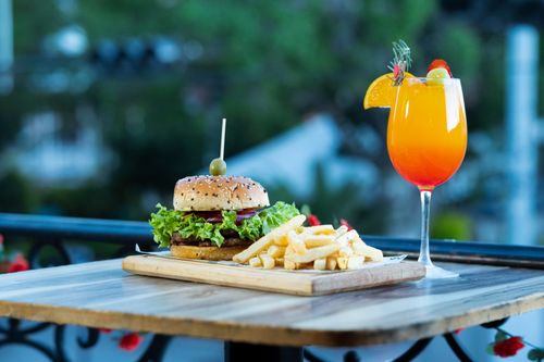 Free Appetizing gourmet burger with fries and a refreshing cocktail served outdoors on a wooden table. Stock Photo