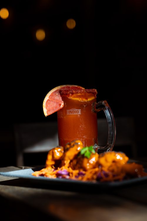 Free Close-up of a Michelada cocktail with grapefruit slice beside spicy chicken wings on a plate. Stock Photo