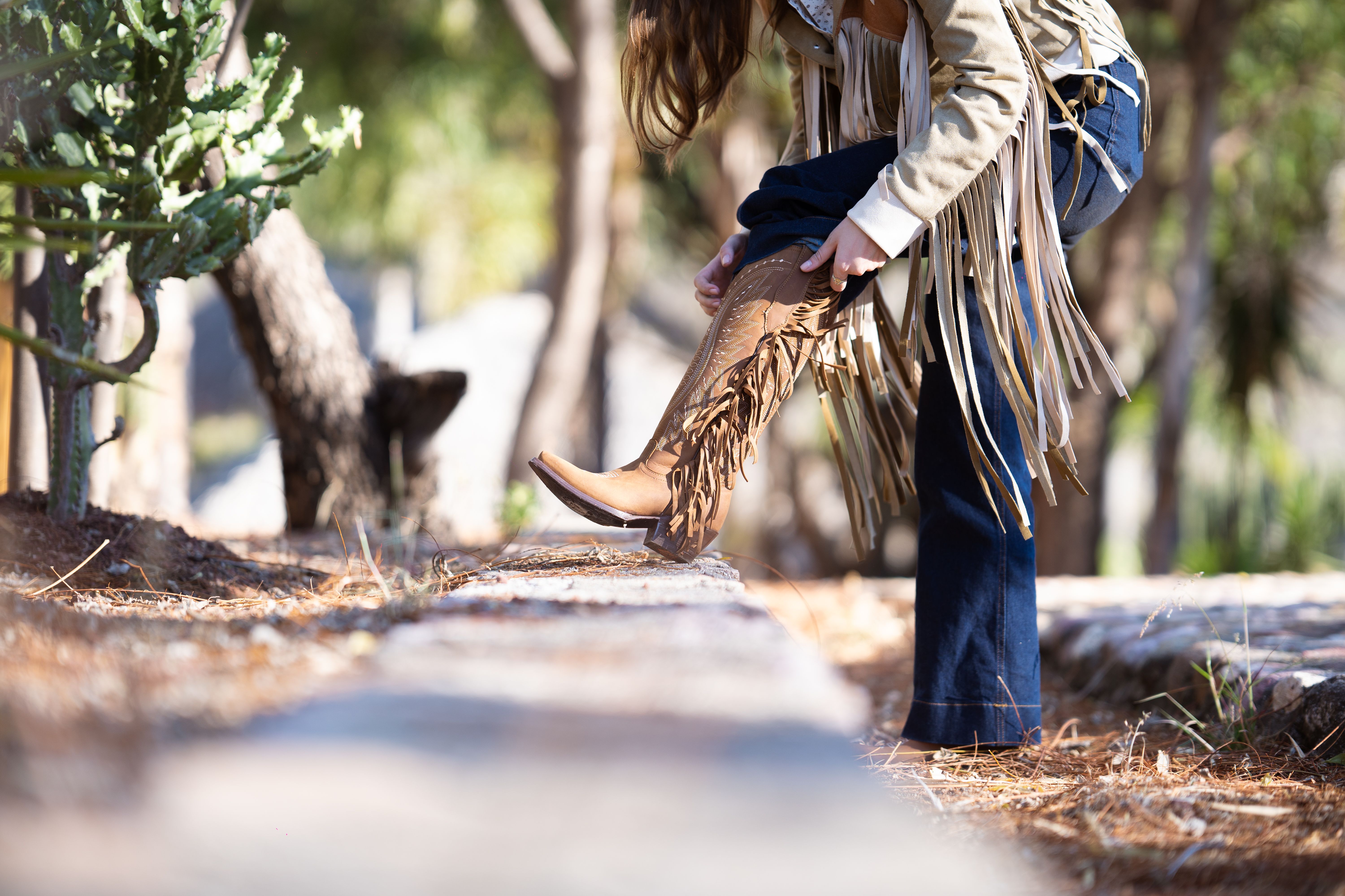 Fashionable cowgirl adjusts fringe boots outdoors, Côte d'Ivoire