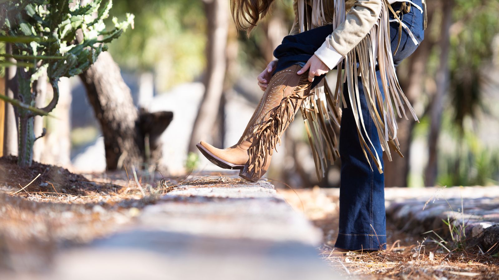 Fashionable cowgirl adjusts fringe boots outdoors, Côte d'Ivoire