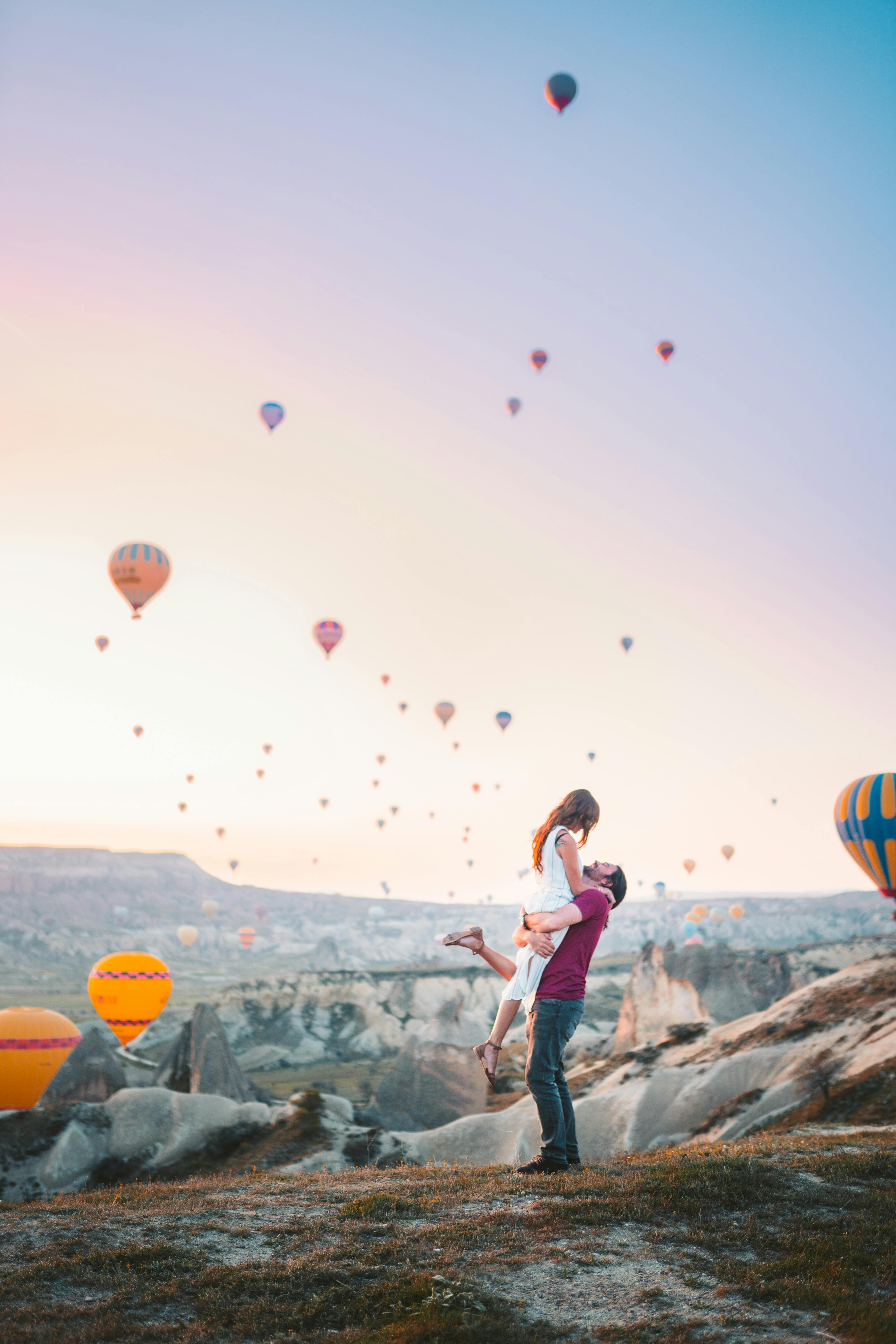 Man Carrying Woman With Hot Air Balloons Background Free Stock Photo