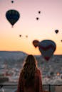 在土耳其卡帕多西亚，一名妇女在日出时分观看热气球，构成了一幅令人惊叹的景色