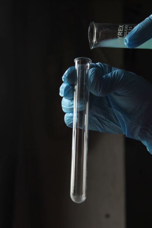 Free Scientist pouring liquid into a test tube, wearing blue gloves, in a dimly lit laboratory. Stock Photo