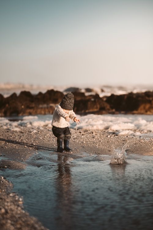 Free A young child joyfully playing by the beach, splashing water on a sunny day. Stock Photo
