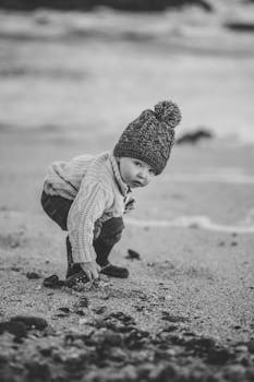 迷人的黑白照片中，一个穿着针织衫的孩子正在海滩探险