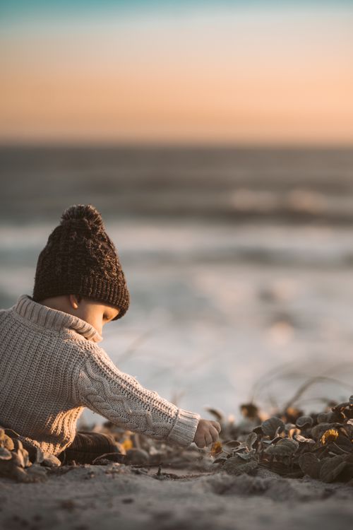 Free A cute toddler in a knitted sweater playing on a sandy beach at sunset. Stock Photo