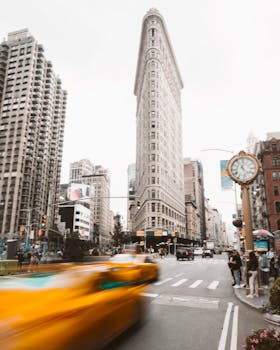 Iconic Flatiron Building with busy street and blurred yellow taxi capturing the essence of New York City.