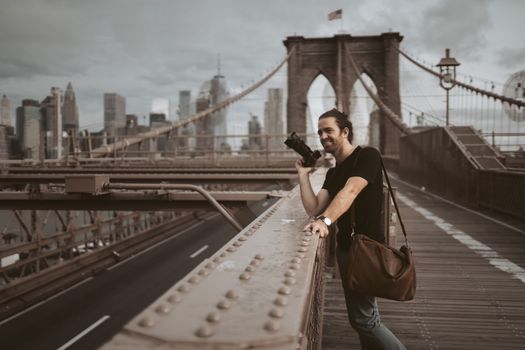 Man photographing on Brooklyn Bridge with New York City skyline in background.