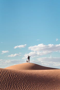 在埃及的沙漠里，一个人影孤独地矗立在蓝天下的沙丘顶上