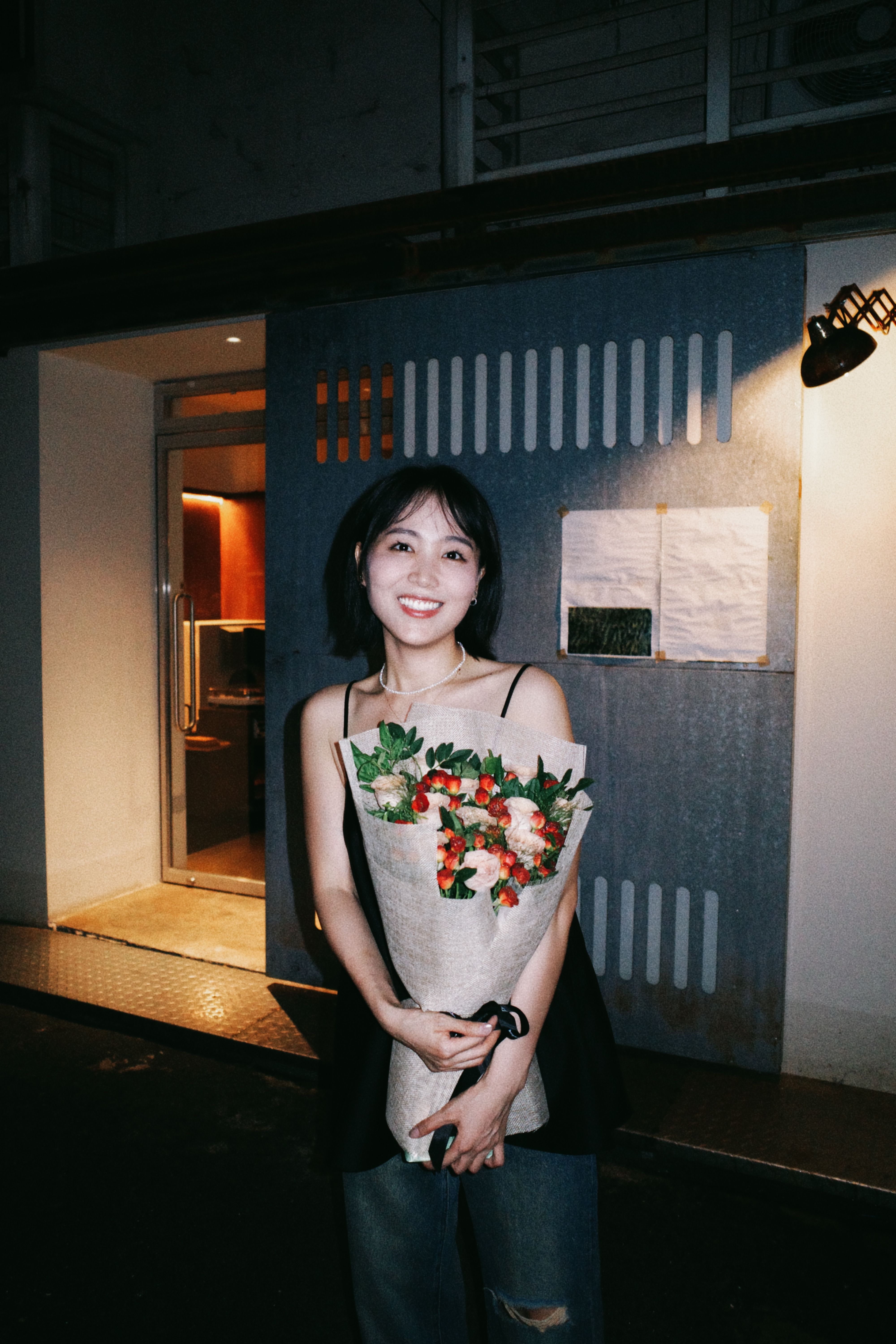 A woman holding a bouquet under outdoor lighting, radiating joy.