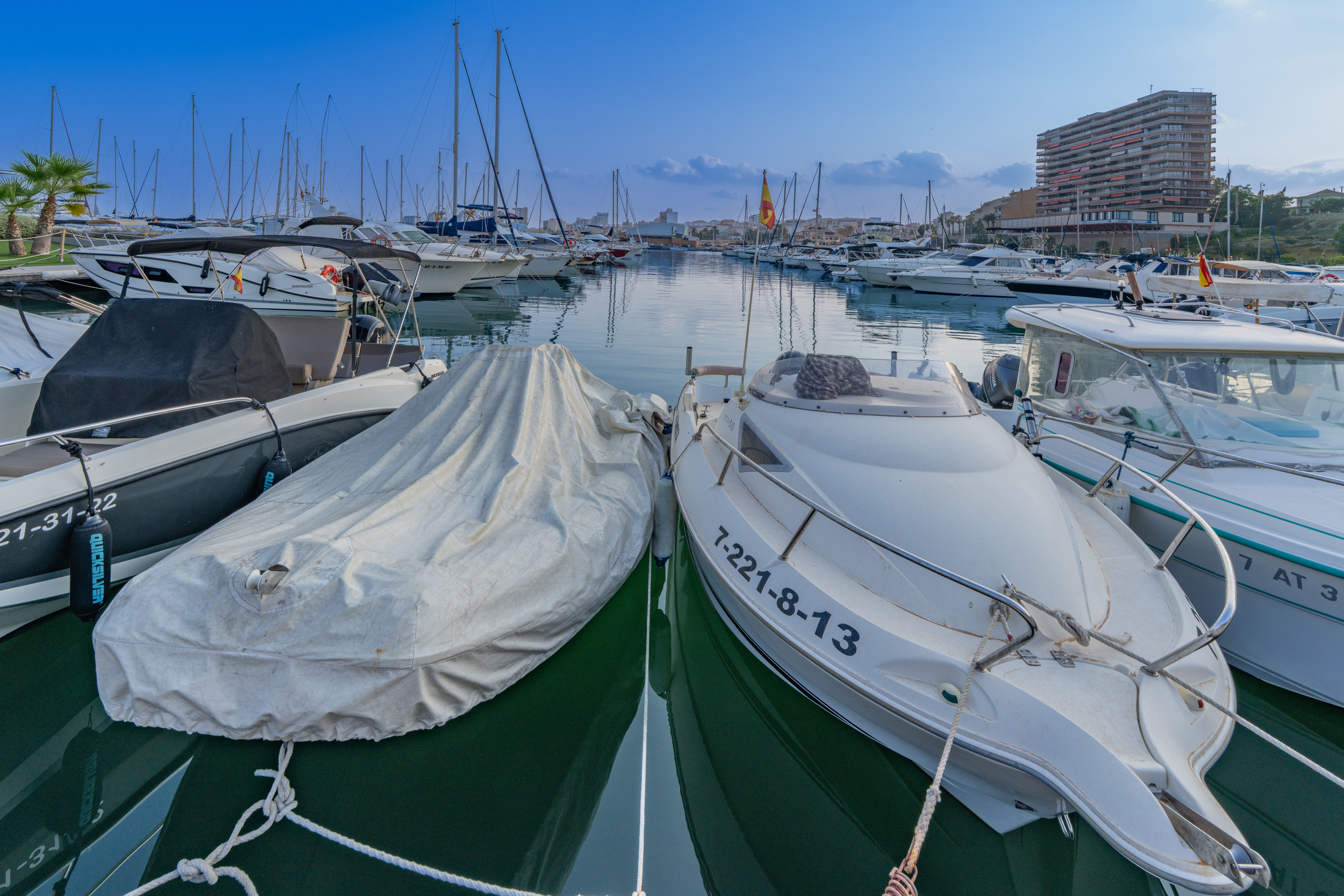 Boats docked at El Campello marina with calm waters and a blue sky backdrop.