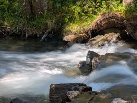 Serene flowing stream in Anterselva di Mezzo, Italy, surrounded by lush greenery and rocks.