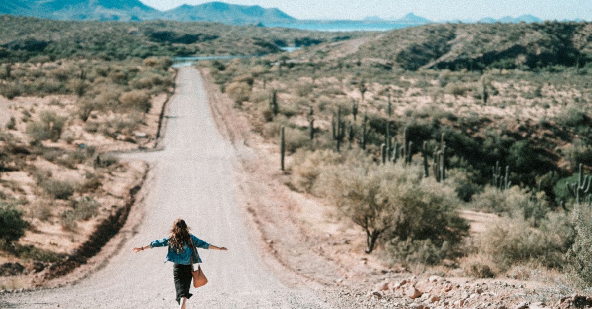 A woman walks freely down a winding desert road in Arizona, embracing adventure.