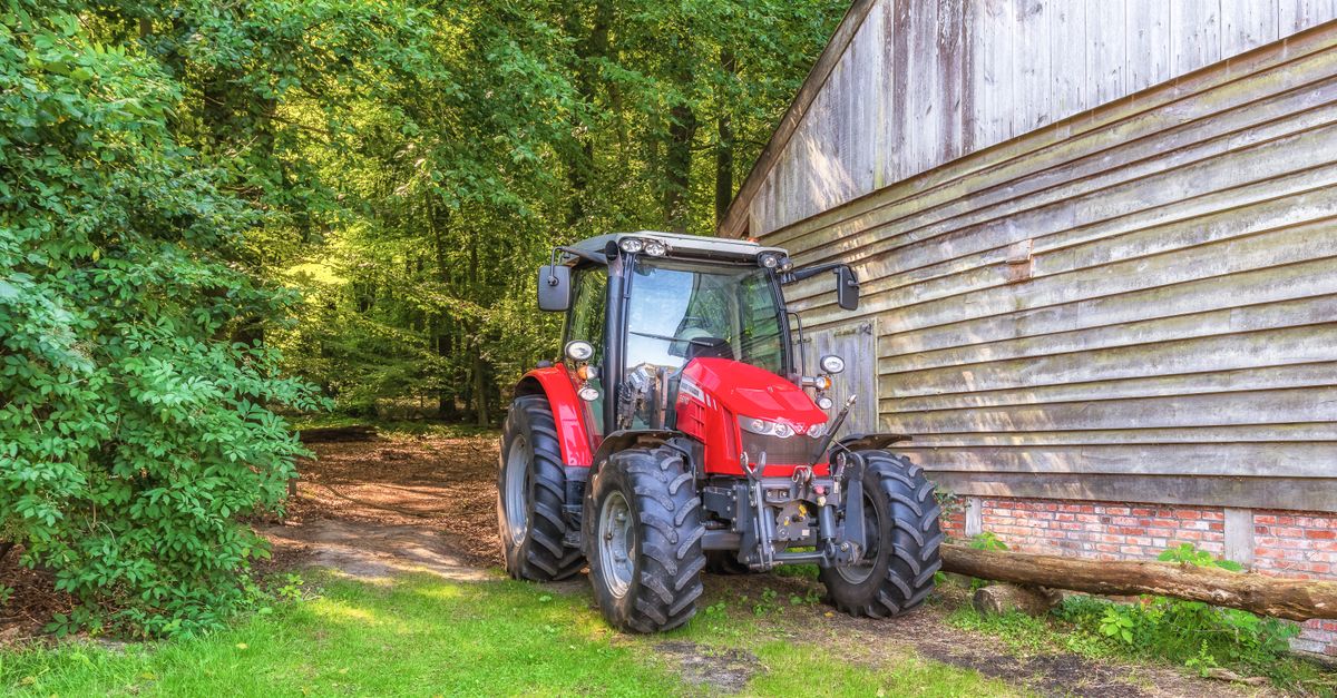 A vibrant red tractor parked beside a rustic wooden barn, surrounded by lush forest.