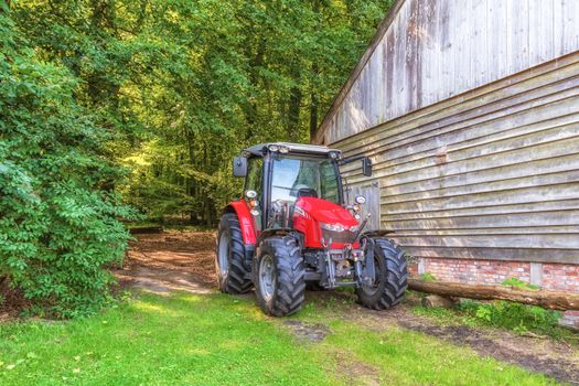 A vibrant red tractor parked beside a rustic wooden barn, surrounded by lush forest.