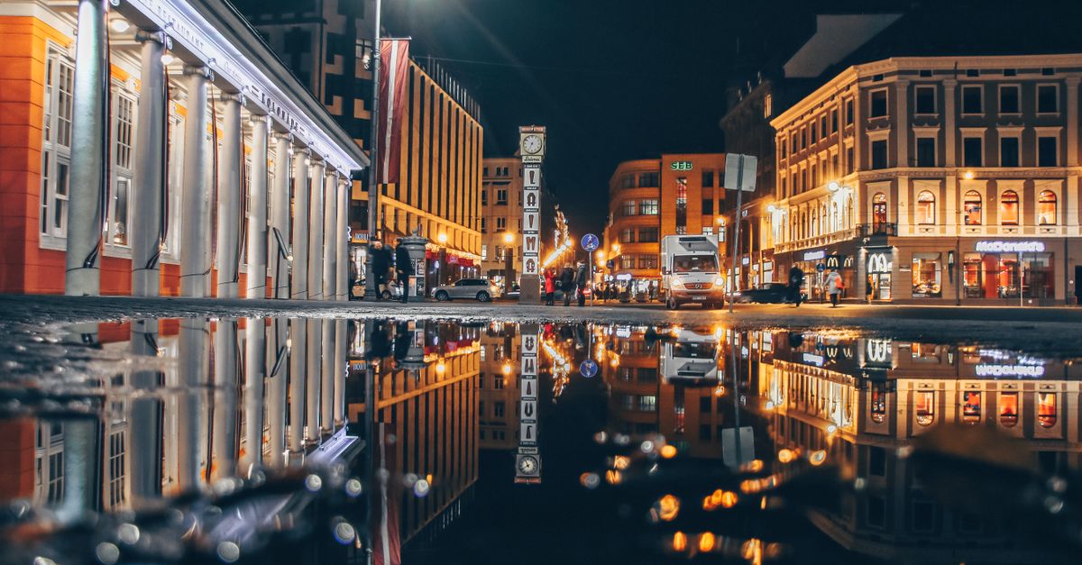 Captivating night view of Riga's city architecture reflected in a puddle, showcasing urban vibrancy.