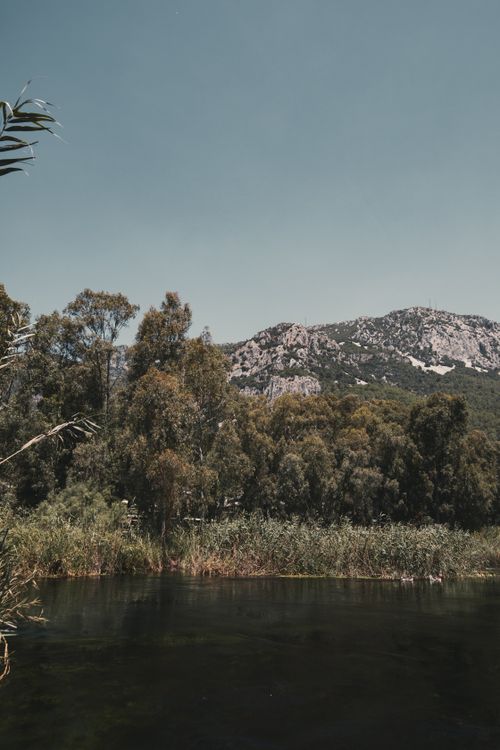 Free Tranquil scene of a mountain with trees and a serene river under a clear sky. Stock Photo