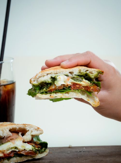 Free Close-up of a hand holding a fresh vegetarian sandwich with a drink in the background. Stock Photo
