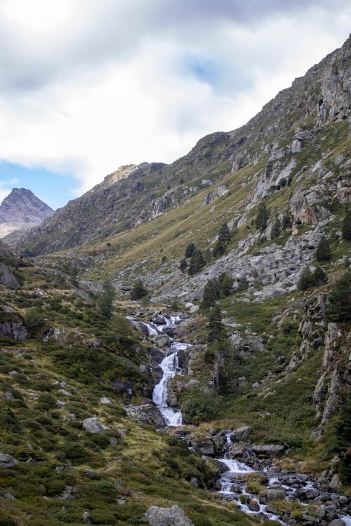 Free Majestic waterfall cascading through a lush alpine valley with rocky terrain. Stock Photo