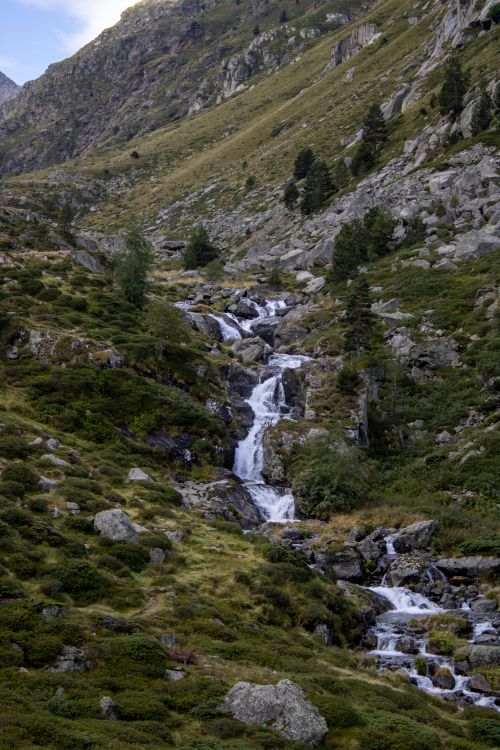 Free A cascading waterfall in a lush Alpine valley surrounded by rocky terrain. Stock Photo
