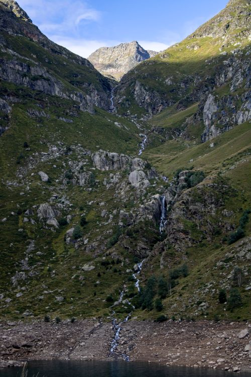 Free Breathtaking mountain landscape featuring a cascading waterfall, lush green terrain, and a serene sky. Stock Photo