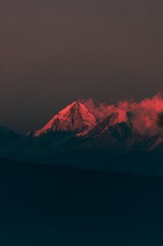 Captivating view of red-lit snow-capped peaks surrounded by clouds during twilight.